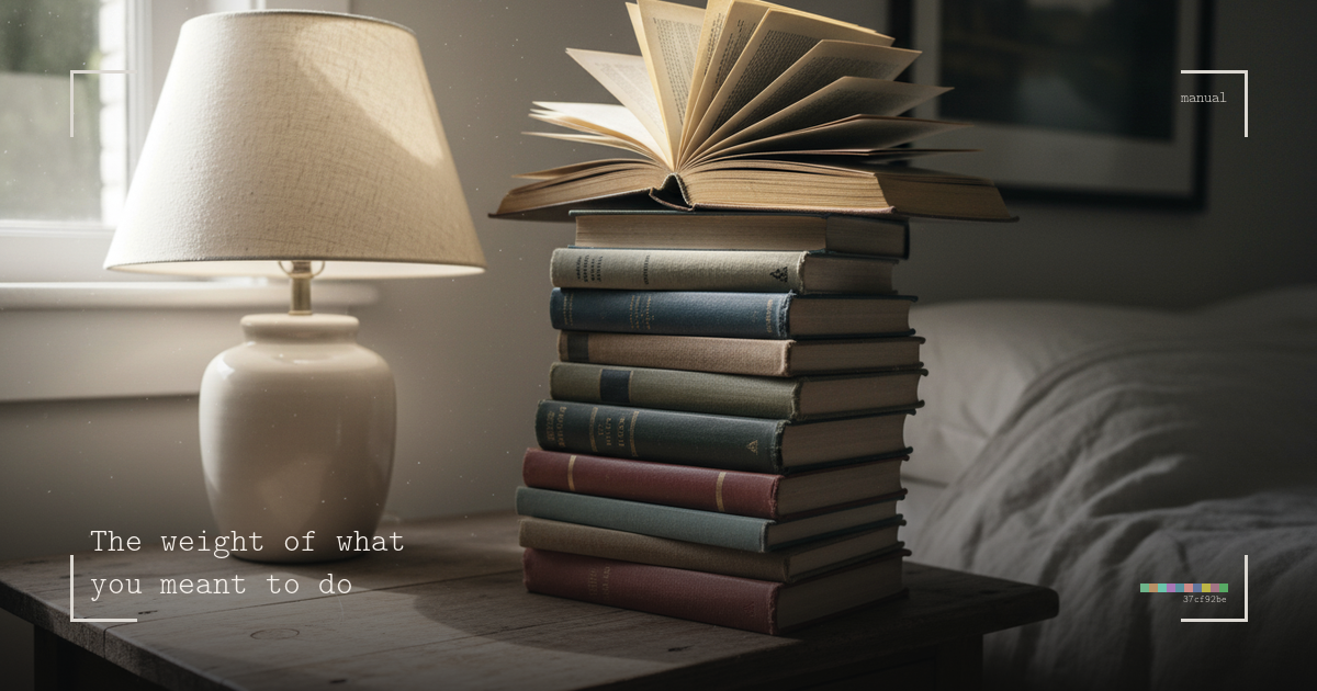 A tall precarious stack of hardcover books on a bedside table, the top book cracked open, a ceramic lamp casting warm light